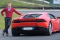 Smiling man posing against red sport car on circuit Royalty Free Stock Photo