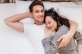 Smiling man posing in bed with wife sleeping on his chest. Indoor overhead photo of chilling couple spending weekend