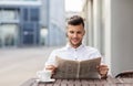 Smiling man reading newspaper at city street cafe