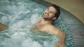 Smiling man relaxing in jacuzzi spa indoor. Sexy guy resting in whirlpool bath Royalty Free Stock Photo