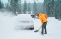 Smiling man with a shovel removing snow from the path and cleaning auto. Car covered with snow as a huge snowdrift on the Royalty Free Stock Photo