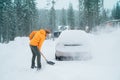 Smiling man with a shovel removing snow from the path and cleaning auto. Car covered with snow as a huge snowdrift on the Royalty Free Stock Photo