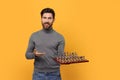 Smiling man showing chessboard with game pieces on yellow background. Space for text Royalty Free Stock Photo