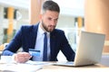 Smiling man sitting in office and pays by credit card with his laptop Royalty Free Stock Photo