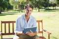 Smiling man sitting on park bench using tablet looking at camera Royalty Free Stock Photo