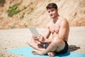 Smiling man sitting and using tablet on the beach Royalty Free Stock Photo