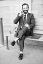 Smiling man in suit sitting on bench and phoning. Handsome smiled young businessman siting on bench with his laptop next to office Royalty Free Stock Photo