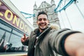 Smiling man taking selfie portrait during travel in London, England - Young tourist male taking memory pic