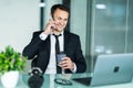 Smiling man talking on mobile phone while using laptop computer at desk Royalty Free Stock Photo