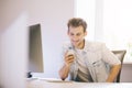 Smiling man talking on mobile phone while using laptop computer at desk in study. Royalty Free Stock Photo