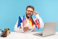 Smiling man teacher adjusting his eyeglasses holding flags of usa, german, great britain and europe countries, advertising foreign