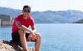Smiling man tourist in a cap rests on the rocks on the seashore. Boka Kotorska bay in Montenegro. Copy space