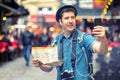 Smiling man tourist in London taking a selfie on crowded streets full of pubs, Happy middle aged male holding city map vlogging Royalty Free Stock Photo