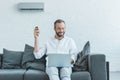 smiling man turning on air conditioner with remote control while using laptop Royalty Free Stock Photo