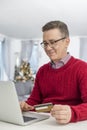 Smiling man using credit card and laptop to shop online at home during Christmas Royalty Free Stock Photo
