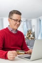 Smiling man using credit card and laptop to shop online at home during Christmas Royalty Free Stock Photo