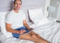 Smiling man using his tablet pc sitting on bed Royalty Free Stock Photo