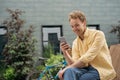 smiling man using mobile phone shopping online, chatting, communication sitting on bench. Young happy freelancer receive payment, Royalty Free Stock Photo