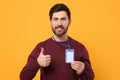 Smiling man with VIP pass badge showing thumbs up on orange background Royalty Free Stock Photo