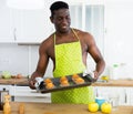 Smiling man wearing only yellow apron holding baking tray with muffins in kitchen Royalty Free Stock Photo