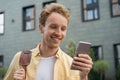 Smiling man wearing yellow shirt using mobile phone, shopping online, reading good news standing on the street. Portrait of happy Royalty Free Stock Photo