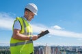 Smiling man in white helmet at construction site writes notes on clipboard Royalty Free Stock Photo