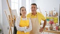 Smiling man and woman artists exuding confidence, standing together with crossed arms gesture amidst vibrant creativity at their