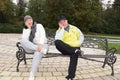 Smiling man and woman sitting on a park bench in the same pose Royalty Free Stock Photo