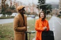 Smiling man and woman in stylish autumn attire holding luggage on urban sidewalk. Royalty Free Stock Photo