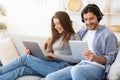 Smiling man and woman using electronic devices, home interior Royalty Free Stock Photo