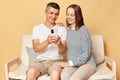 Smiling man and woman wearing casual clothing using mobile phone watching videos browsing internet together sitting on clothes Royalty Free Stock Photo