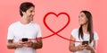 A smiling man and woman in white t-shirts are texting on smartphones, connected by a looping red heart line Royalty Free Stock Photo