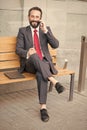 Smiling manager sitting on bench and phoning. Handsome smiled young businessman siting on bench with his laptop next to office