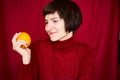 Smiling mature brunette woman looking at orange fruit in hand, close-up face portrait. Generation X,