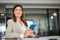 Smiling mature business woman holding phone looking away in office. Royalty Free Stock Photo