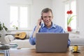 Smiling mature businessman talking on mobile phone while working in home office with his laptop Royalty Free Stock Photo