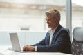 Smiling Mature businessman workingon laptop while sitting in modern coworking