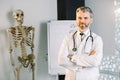 Smiling mature Caucasian man doctor posing with arms crossed in the office, wearing white coat and stethoscope, human Royalty Free Stock Photo