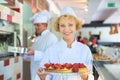 Portrait of smiling mature chef holding fresh strawberry tarts in tray at restaurant