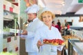 Portrait of smiling mature chef holding fresh strawberry tarts in tray at restaurant