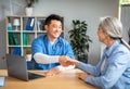 Smiling mature chinese man doctor shaking hands with elderly caucasian woman patient in clinic office Royalty Free Stock Photo