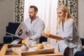 smiling mature couple in bathrobes holding newspaper and smartphone while having breakfast in hotel