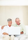 Smiling mature couple using laptop on couch. Smiling mature couple using laptop while sitting on couch. Royalty Free Stock Photo