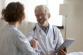 Smiling mature doctor shaking woman hand, holding digital tablet