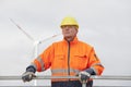 Smiling mature engineer with hard hat and protective clothing in front of blurred wind turbine