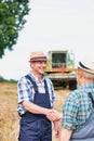 Smiling mature farmer shaking hands with senior farmer in field against harvester Royalty Free Stock Photo