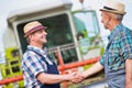 Smiling mature farmer shaking hands with senior farmer in field against harvester Royalty Free Stock Photo