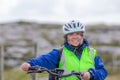 Smiling mature female cyclist with a blue jacket, helmet and anti-reflective vest next to a bicycle