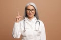 Smiling mature gray-haired Asian female doctor points finger up Royalty Free Stock Photo