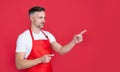 smiling mature houseman in apron on red background. pointing finger